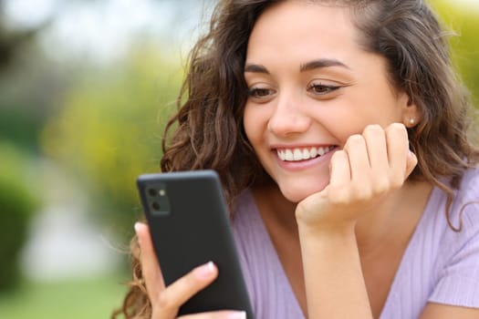 Happy woman checking smart phone smiling in a park
