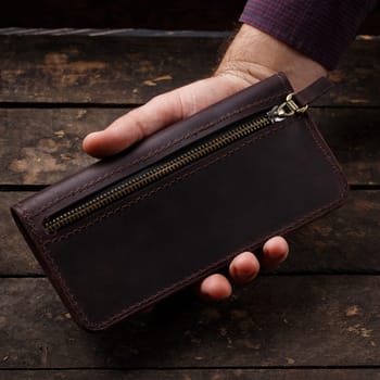 Leather brown men's wallet in a man's hand on a vintage wooden background. Flat lay. Place for text. Copyspace