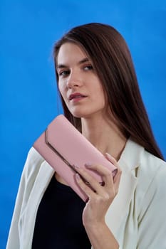 A beautiful young woman is holding a pink purse on a blue background, copy space. High quality photo