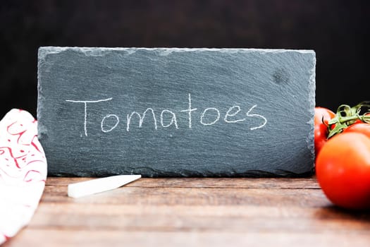 Fresh tomatoes and a chalkboard sign with tomatoes written on it.