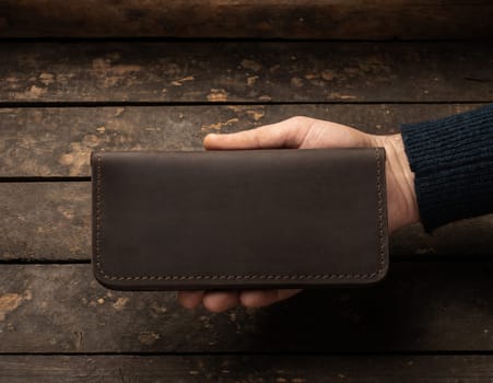 Leather men's wallet in a man's hand on a vintage wooden background. Flat lay. Place for text. Copyspace