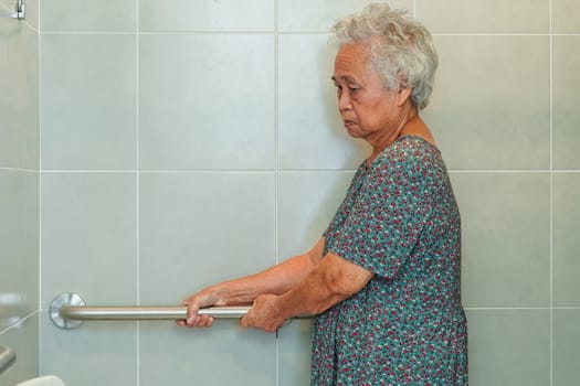 Asian elderly old woman patient use toilet support rail in bathroom, handrail safety grab bar, security in nursing hospital.