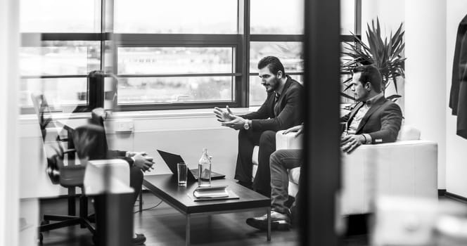 Businessmen interviewing female candidate for job in modern corporate office. Woman during job interview and two elegant members of management. Through glass view, black and white.