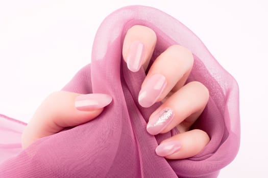 Female hand with shiny pink rose nails is holding a pink decoration on white background, nail care and manicure concept.