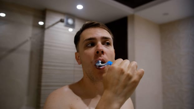 Young man brushing his teeth in bathroom. Beautiful interior.