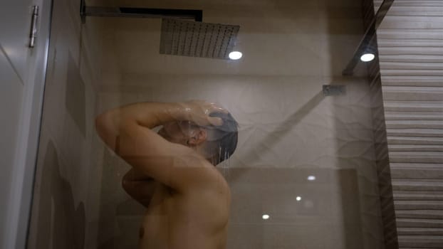 Man taking a shower washing hair under water falling from rain showerhead. Showering person at home lifestyle. Young adult body care morning routine