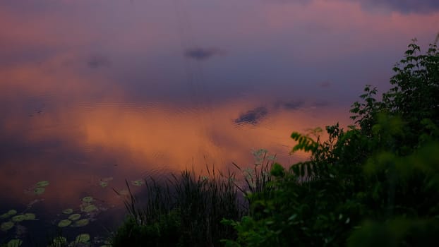 Cloudscape in summer at sunset on the lake and field