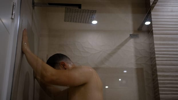 Man taking a shower washing hair under water falling from rain showerhead. Showering person at home lifestyle. Young adult body care morning routine