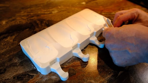 Making homemade popsicles. man pouring ice cream in freezer molds and put a stick inside