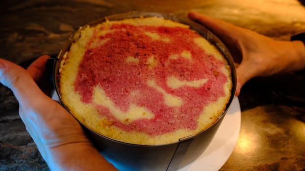 man take out metal round shape on creamy biscuit on table, close-up cooking cake.