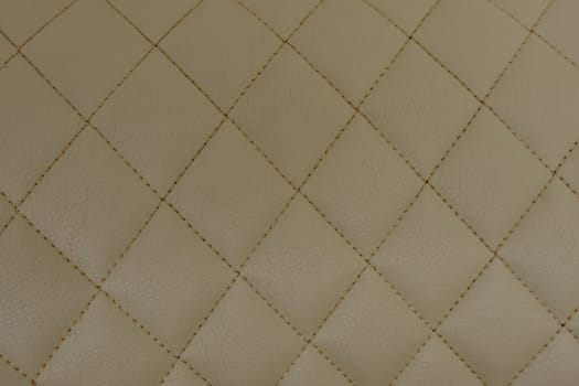 Background of beige leather quilted in the form of rhombuses.