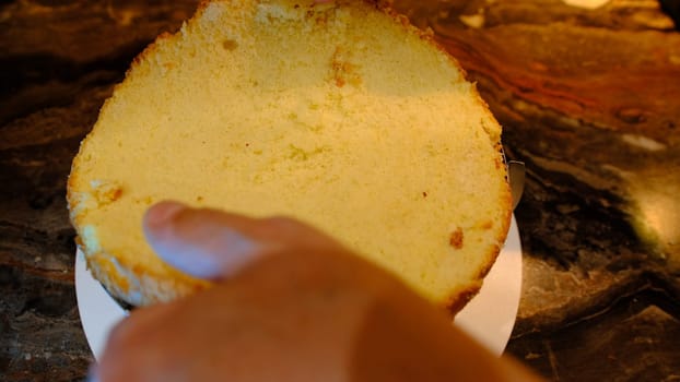 a male pastry chef puts a cake on cream with cherry and press it. Slaps and flattens the sponge cake close up.