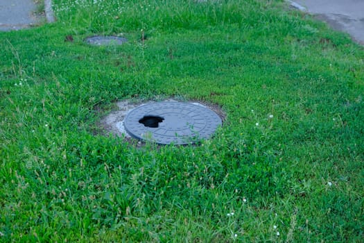 broken cast-iron manhole among the grass in park. Manhole with a hole.