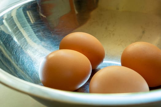 Raw eggs in shells in a silver bowl, close up