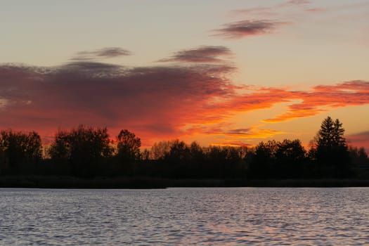 Orange red clouds after sunset over trees and lake