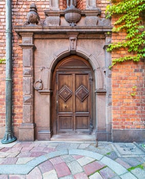 Ornamental wooden arched door framed by engraved marbles in a red brick wall and colorful cobblestone tiled floor at Stockholm City Hall, Sweden