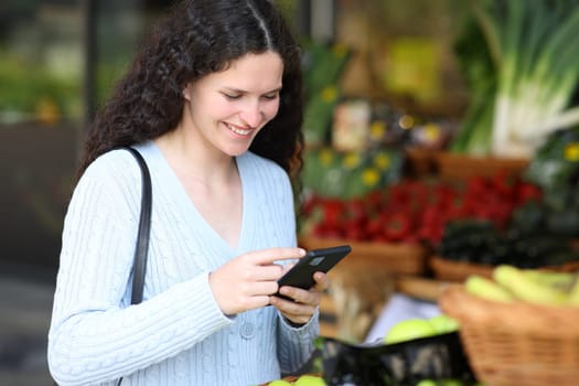 Customer using smart phone standing in a greengrocery