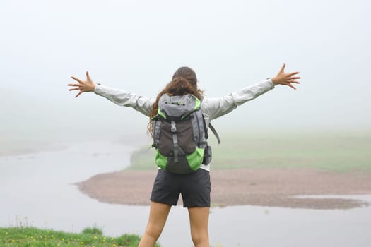 Back view portrait of a hiker outstretching arms in the mountain a foggy day