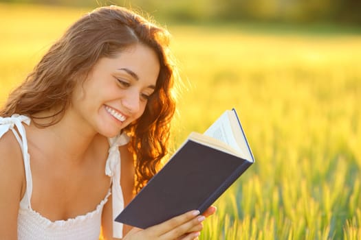 Happy woman reading a book smiling in a wheat field at sunset
