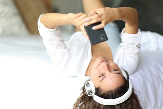 Happy woman listening to music wearing headphones on a bed