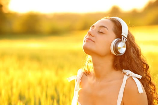 Relaxed woman meditating with wireless headphones in a wheat field at sunset