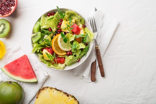 Fresh salad with fruits and greens on white background top view with space for text. Healthy food.