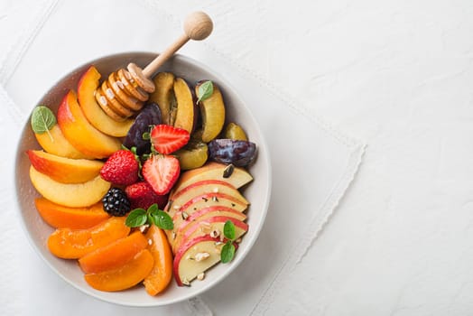 Bowl of healthy fresh fruit salad sweetened with honey on white background