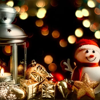 Christmas composition: A snowman, a lantern with candles, bright shiny boxes with gifts, blurred bokeh lights in the background.