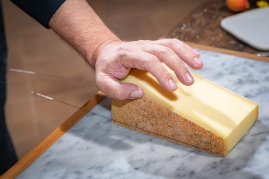 A man cuts a portion of The Gruyère with a wire, the famous swiss cheese in a cellar on a marbble background