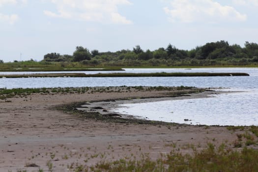 Water surface with small sand island, blue sky in background.Wasserfläche mit kleiner Sandinsel, blauer Himmel im Hintergrund.