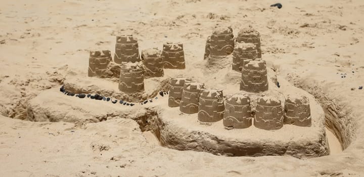 A sandcastle, blob castle built on a beach with childrens toys.