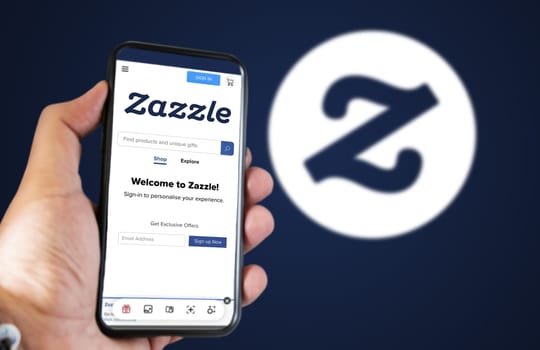 San Francisco, USA, June 2022: hand holding a phone with Zazzle homepage on the screen. Zazzle logo blurred on a blue background. Zazzle is an American online marketplace