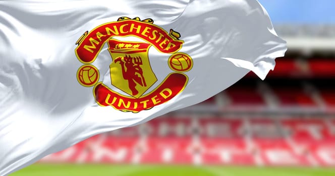 Manchester, UK, May 2022: The flag of Manchester United waving with Old Trafford stadium blurred in background.