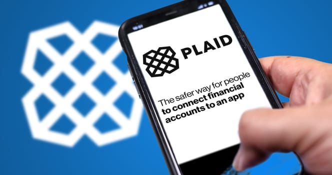 San Francisco, USA, June 2022: hand holding a phone with Plaid homepage on screen. Plaid logo blurred on a blue background. Plaid is a financial services company based in San Francisco