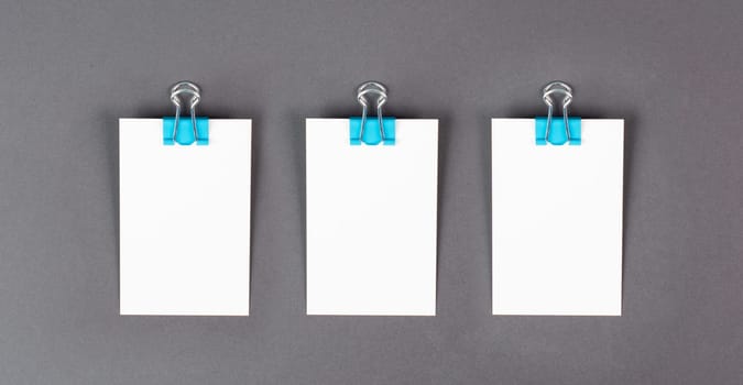 Blank white paper with a paperclip on a gray colored background, copy space for text, reminder or message in the office, communication concept