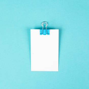 Blank white paper with a paperclip on a blue colored background, copy space for text, reminder or message in the office, communication concept