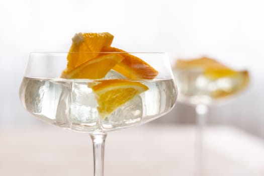 Transparent cocktail with ice cubes in a champagne coupe glass decorated with slices of orange close up. Tropical drink at the bar. Summer vacation mood