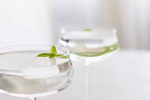Transparent cocktail with ice cubes in a glass decorated with mint leaves close up. Tropical drink at the bar. Summer vacation mood. Analcolic mocktail drink