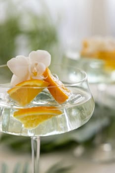 Exotic Cocktail with ice cubes in a coupe glass decorated with slices of orange and orchid flower close up. Tropical drink at the bar outdoor. Summer vacation mood