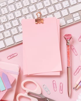 Paper with a clip, Pink school accessories and keyboard on light pink, Top view, mockup. Girly workplace with notebook, scissors, pencil, pen, paperclips and card. Back to school