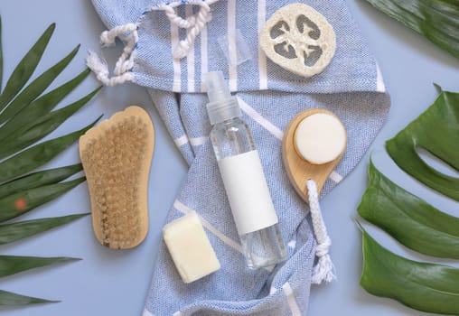 One pump dispenser, skin and hair care accessories on blue bath towel near tropical leaves top view, copy space. Packaging mockup. Natural homemade products