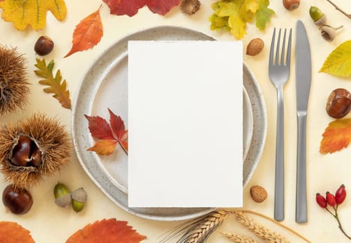 Autumn table place with colorful leaves and blank card top view. Mockup of fall vertical card on light yellowtable, flat lay, copy space. Harvest, Halloween and Thanksgiving season