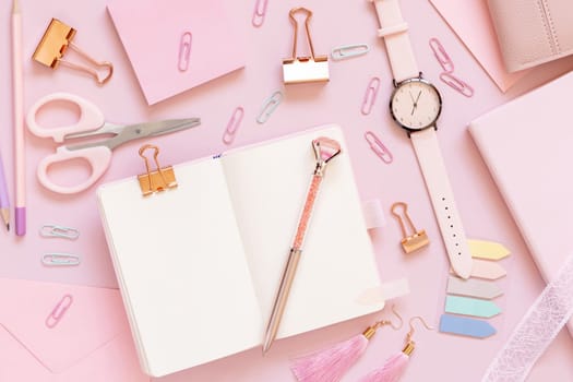 Opened notebook and Pink school accessories on pastel pink, Top view, textbook mockup. Girly workplace with scissors, pencils, pen, paperclips, earrings and watch. Back to school concept