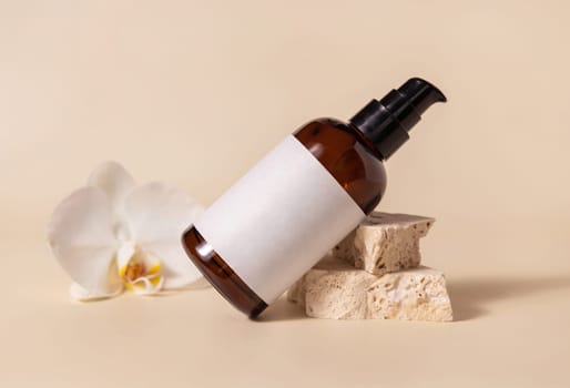 Brown glass one pump bottle near white orchid flower and beige stones on light yellow close up, mockup. Skincare beauty product package. Natural cosmetics, minimal composition..
