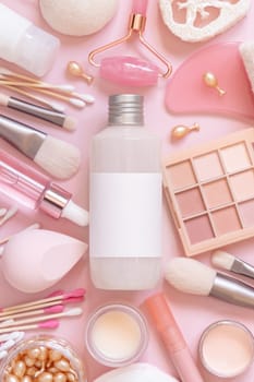 Bottle with blanik label, skin care and decorative cosmetics on pink, top view, mockup. Flat lay with natural beauty products and decorative cosmetics. Everyday woman face care routine