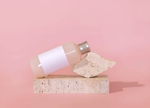 Bottle with blank label lies lies on travertine stone on light pink, close up, mockup. Skincare beauty product. Natural cosmetics, lotion or cleanser. Minimal composition..