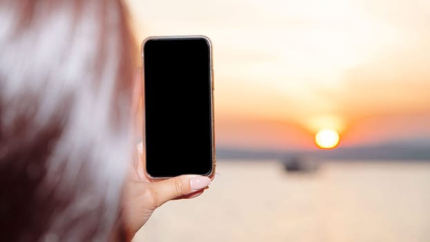 Young woman holding smart phone with mockup black blank display, empty screen for social media app ads at home. Mobile applications technology concept.