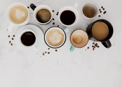 Top view on flat lay with many different full and empty coffee cups composition on gray white concrete background. Variety of tea mug collection layout. Dried coffee beans. Espresso, latte, americano