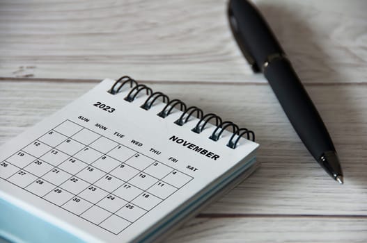 November 2023 white desk calendar with black pen on wooden table. Calendar concept