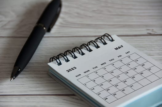 May 2023 white desk calendar with black pen on wooden table. Calendar concept